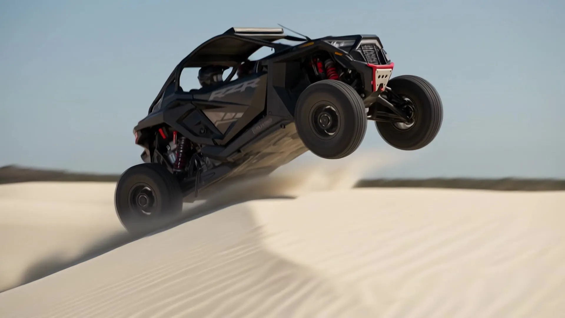Black Polaris RZR cresting a jump over midday sand dunes